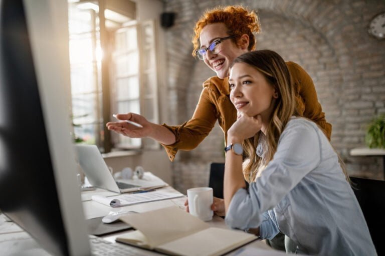 happy-female-entrepreneurs-reading-email-computer-while-working-together-office-focus-is-redhead-woman